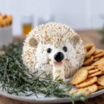 Hedgehog-shaped cheeseball covered with sliced almonds and decorated with olive eyes.